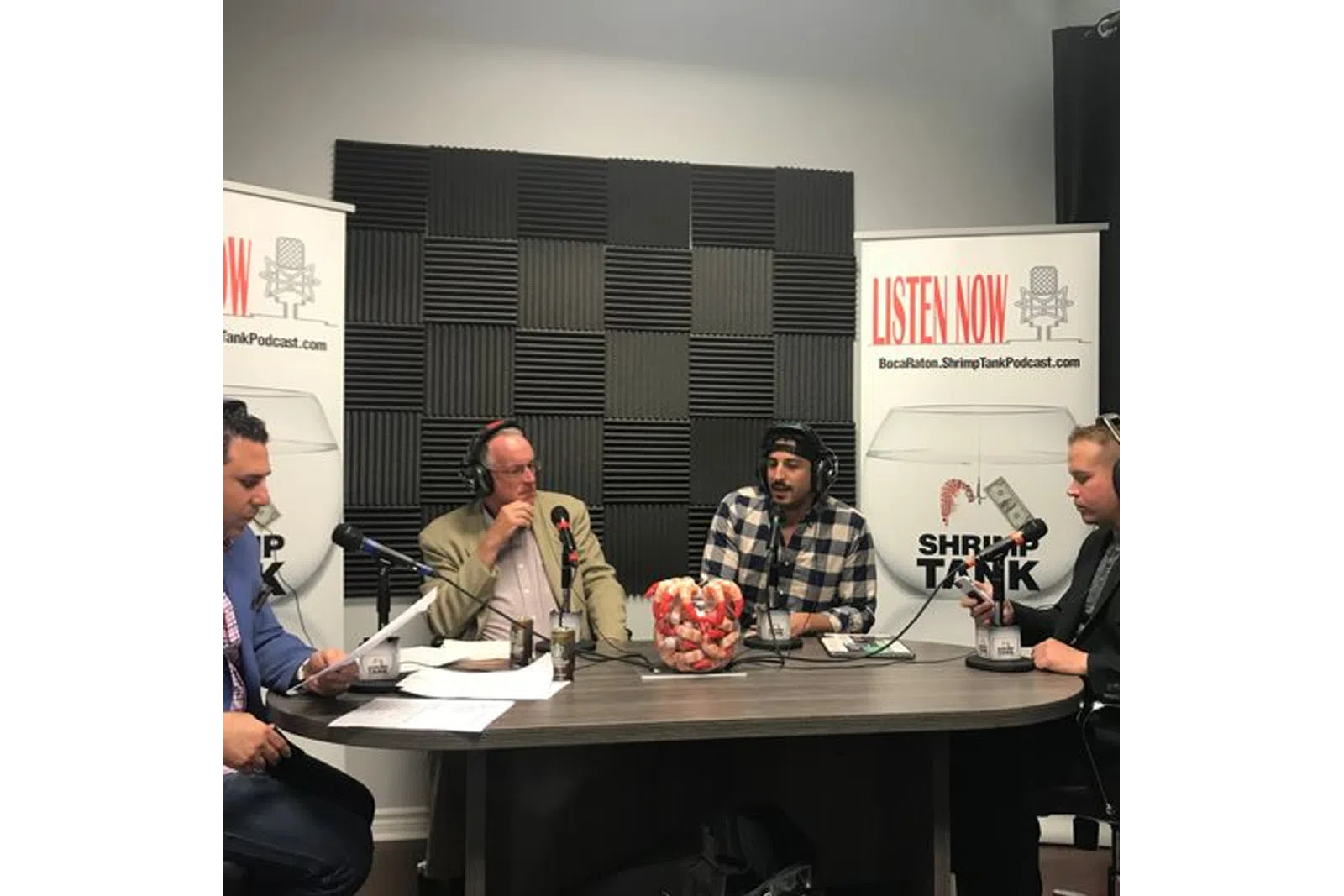 a group of men sitting at a table with microphones and a sign