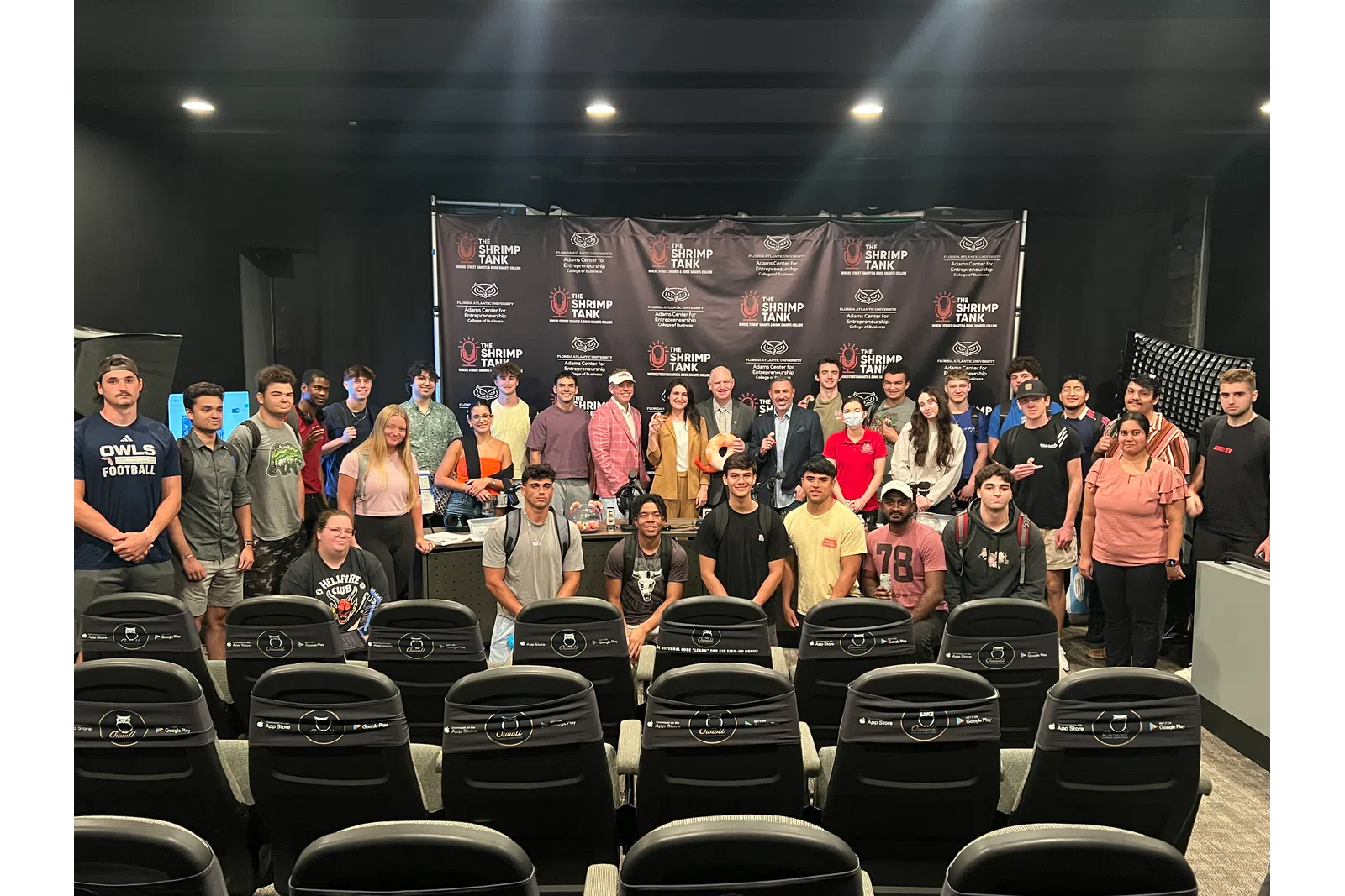 Group of diverse young adults and instructors posing in front of a Shrimp Tank event backdrop in a conference room.