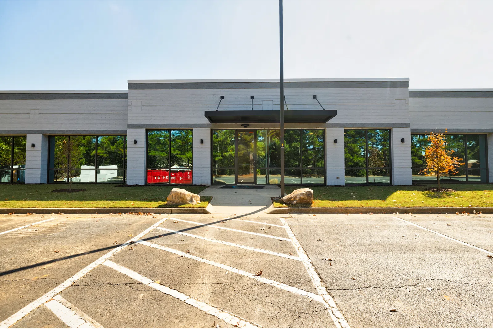 Empty parking lot in front of a modern commercial building with glass doors and windows on a sunny day