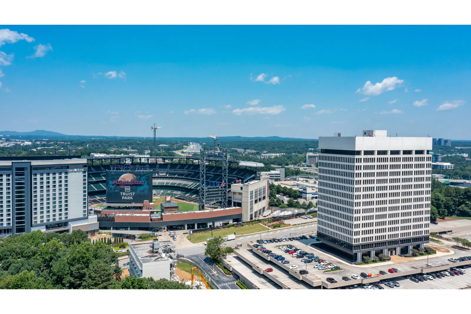 Aerial view of Truist Park baseball stadium with surrounding buildings and parking lots under blue sky.