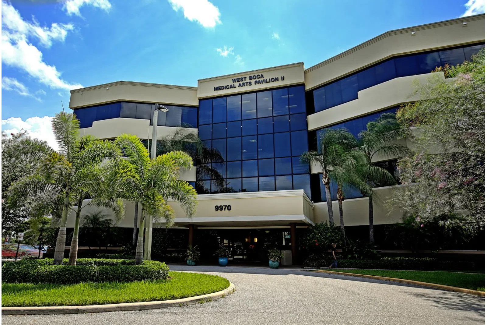 Modern three-story medical office building with palm trees and blue sky at West Boca Medical Arts Pavilion