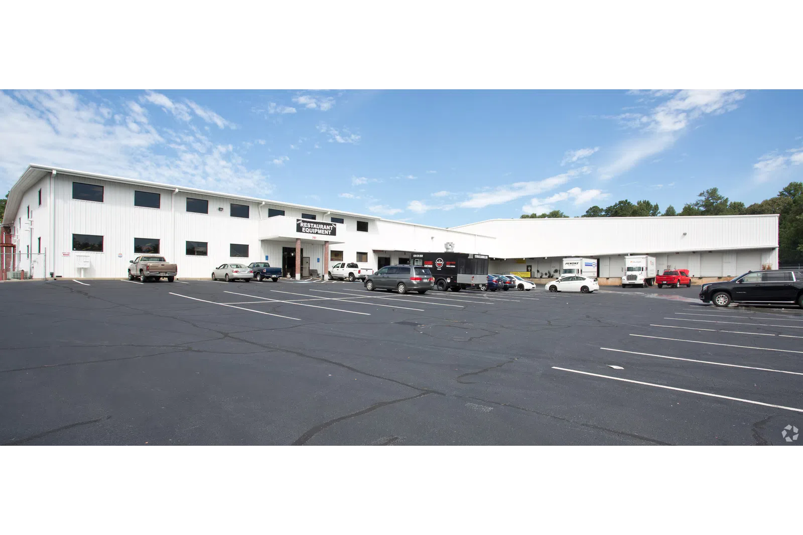Large white commercial building with restaurant equipment sign and parked vehicles under blue sky.