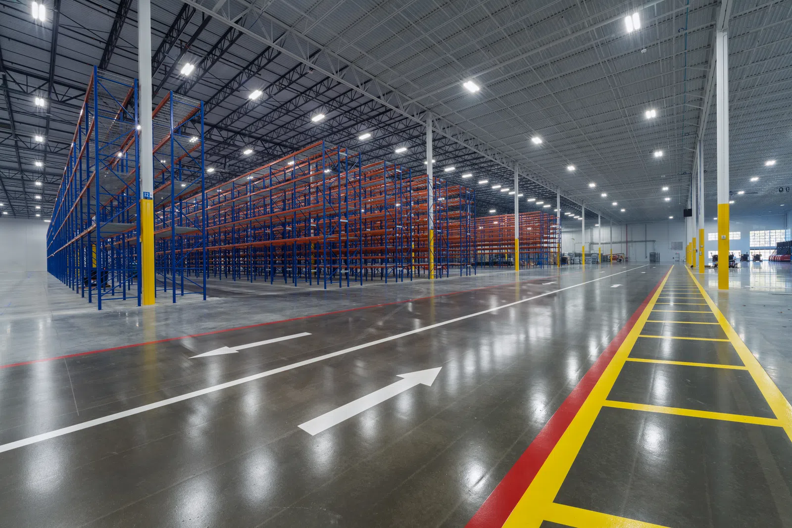 Empty spacious warehouse with tall blue and orange shelving and marked polished concrete floors