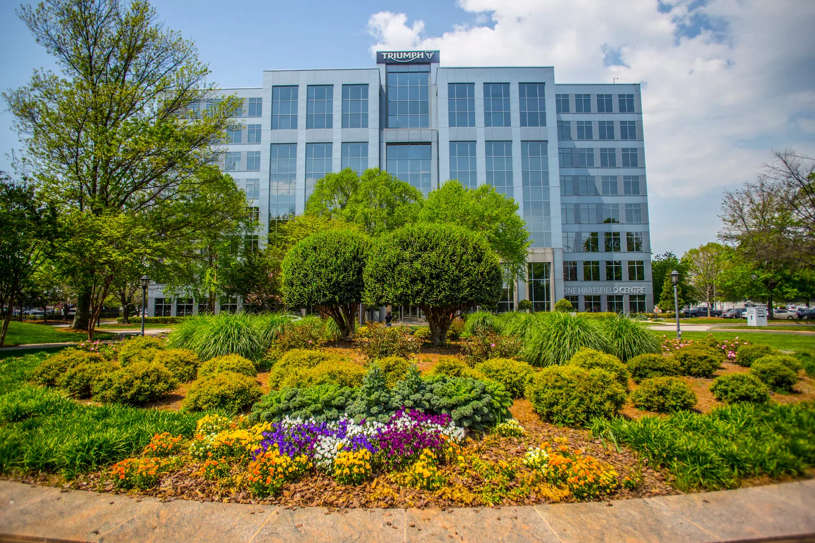 Modern glass office building behind a landscaped garden with colorful flowers and green shrubs under a blue sky