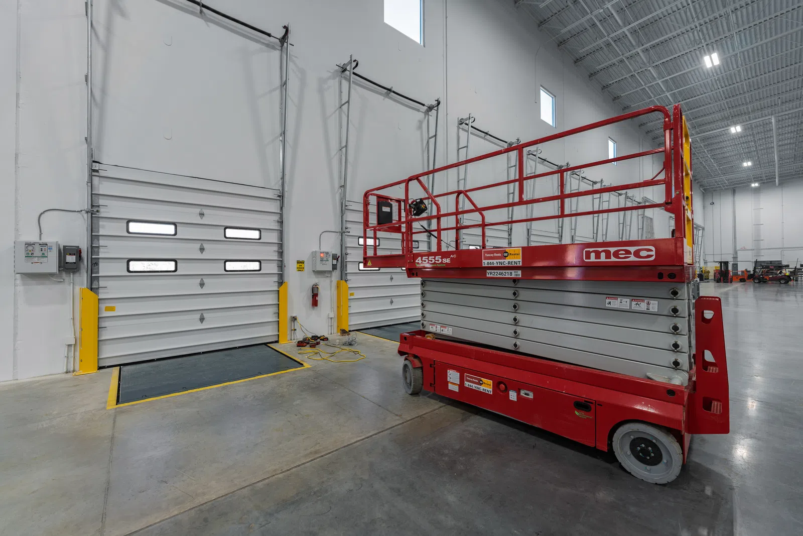 Red MEC scissor lift parked inside a large industrial warehouse near loading dock doors.