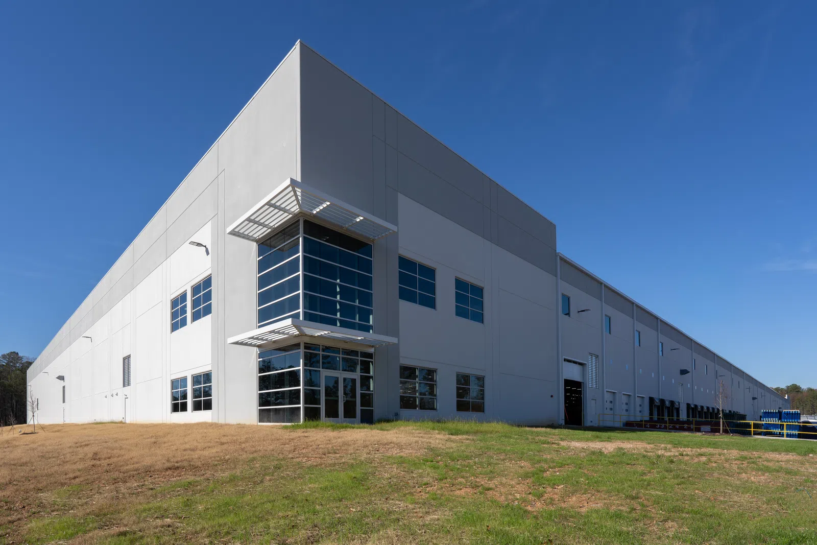 Modern large industrial warehouse building with glass entrance under clear blue sky on grassy land