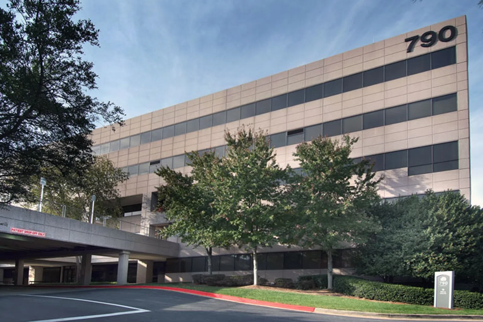 Modern office building with reflective windows, trees, and a parking entrance under a blue sky, number 790 visible