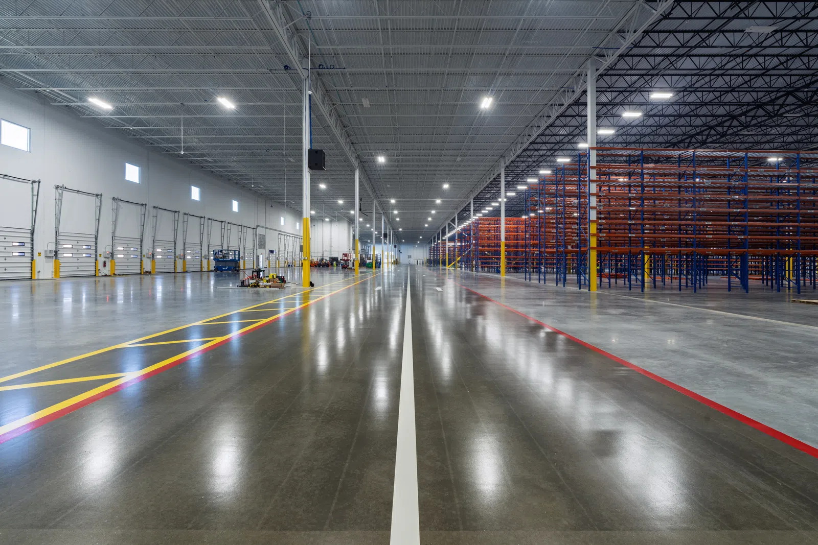 Spacious industrial warehouse with empty shelving units and polished concrete floors under bright LED lighting.