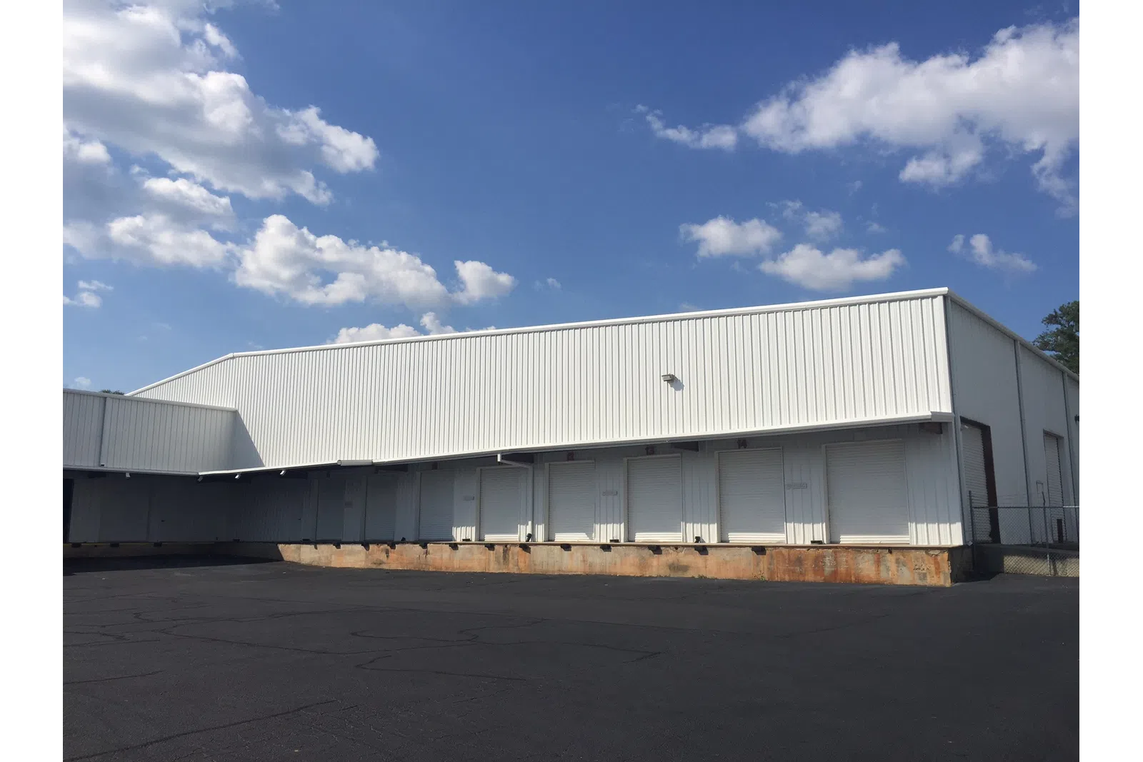 White industrial warehouse with multiple loading dock doors under a partly cloudy blue sky.