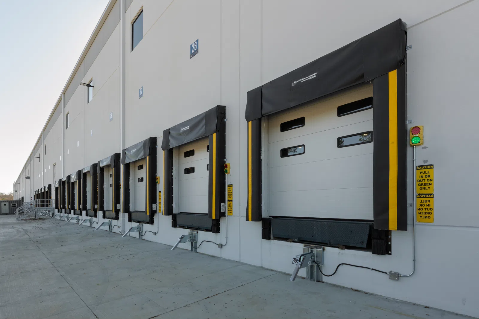Row of modern loading dock doors with protective seals on industrial warehouse exterior under clear sky.