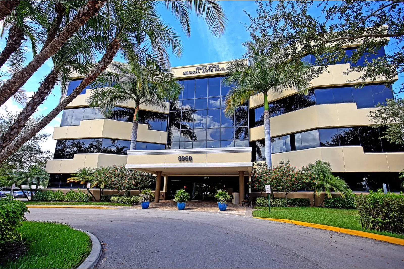 Modern three-story medical arts pavilion with palm trees and a reflective glass facade under a blue sky.