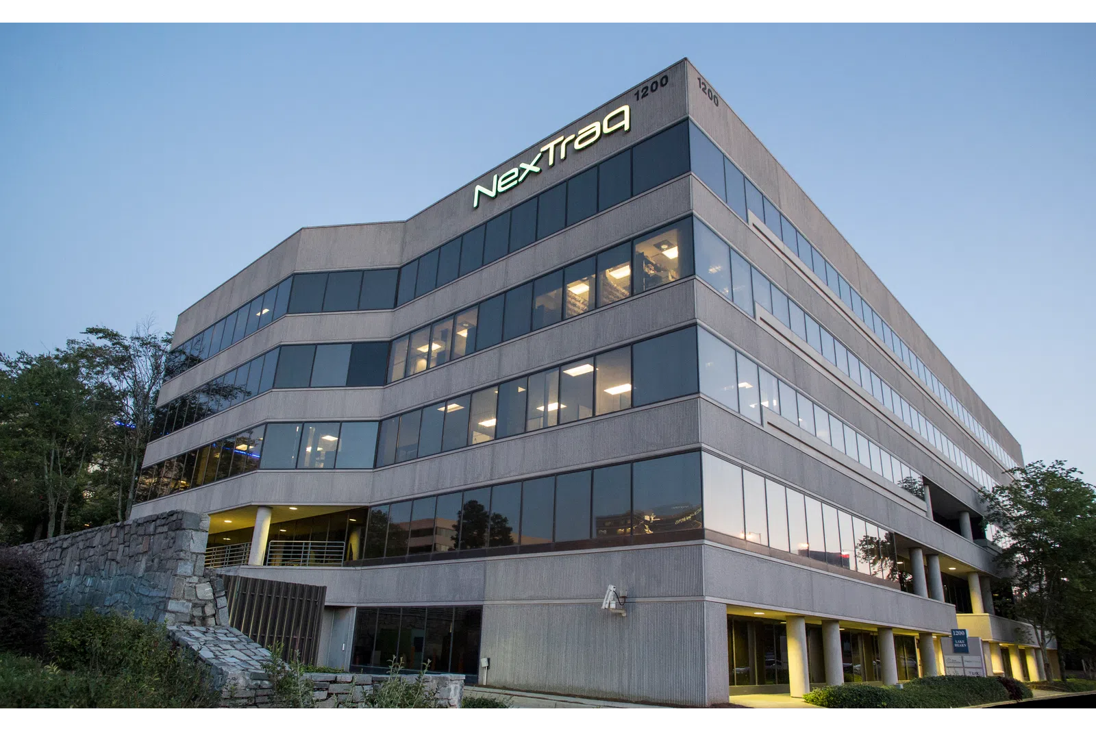 Modern office building of NexTraq with illuminated logo at the top corner during early evening.