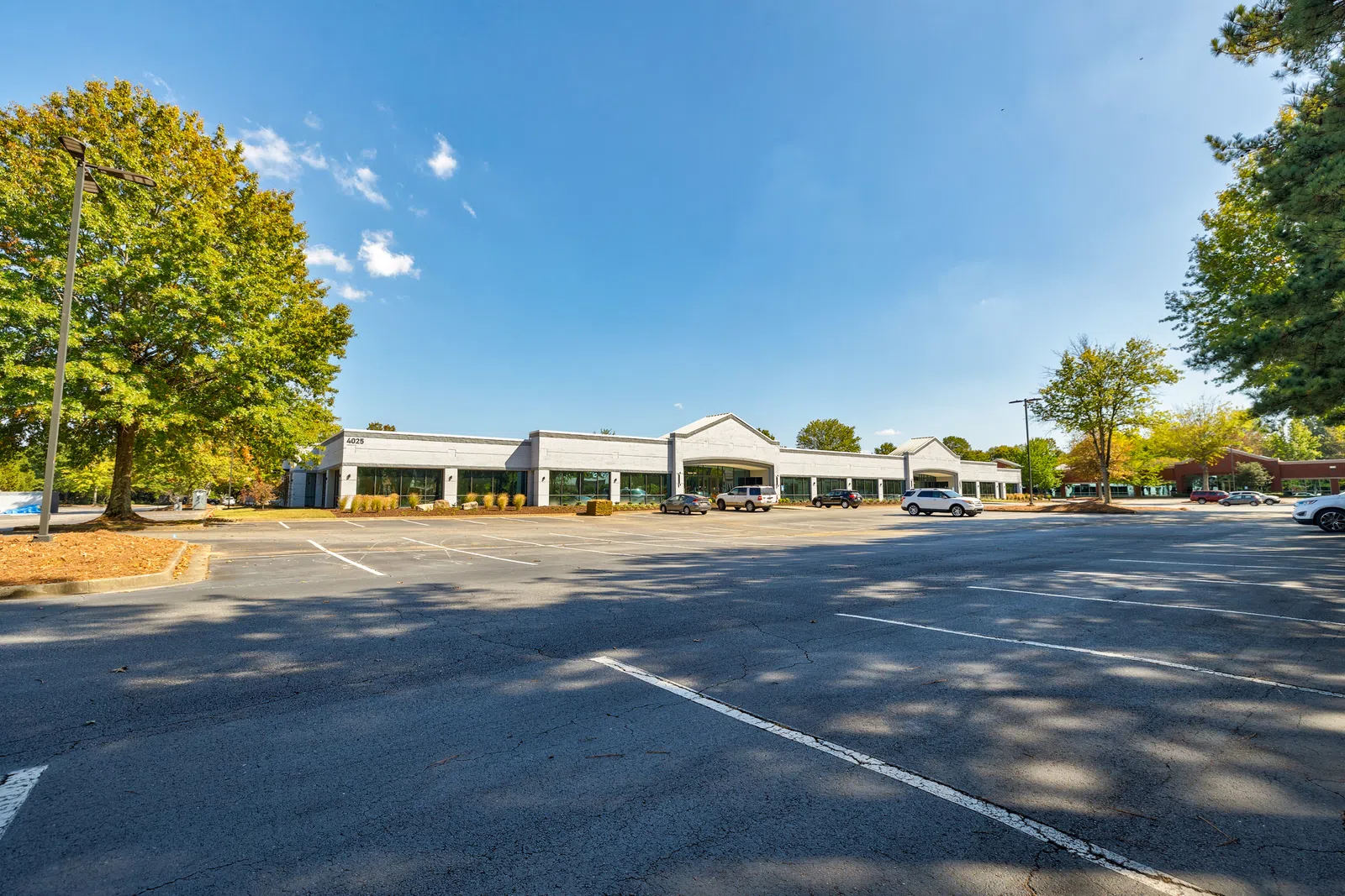 Spacious parking lot with few cars in front of a single-story commercial building under blue sky