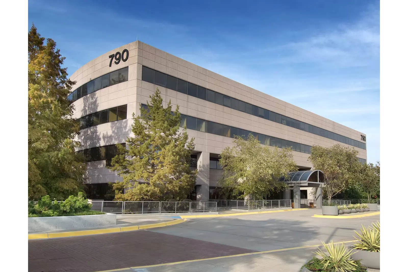 Modern office building with large windows, trees, and clear blue sky at 790 address.