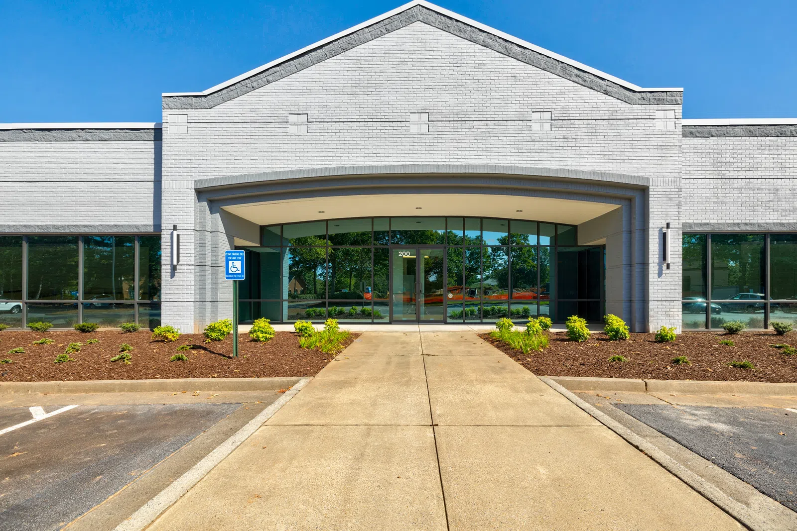 Modern commercial building front with wide entrance, large windows, and clear blue sky.