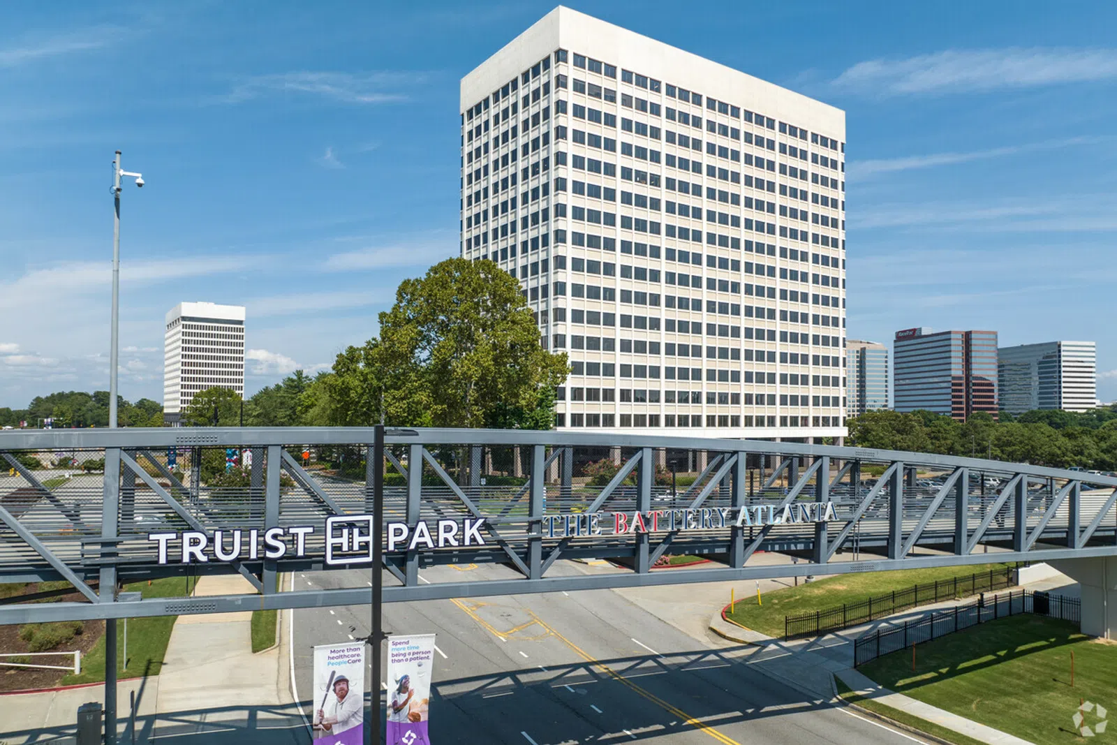 Truist Park sign on a pedestrian bridge with office buildings and clear blue sky in the background