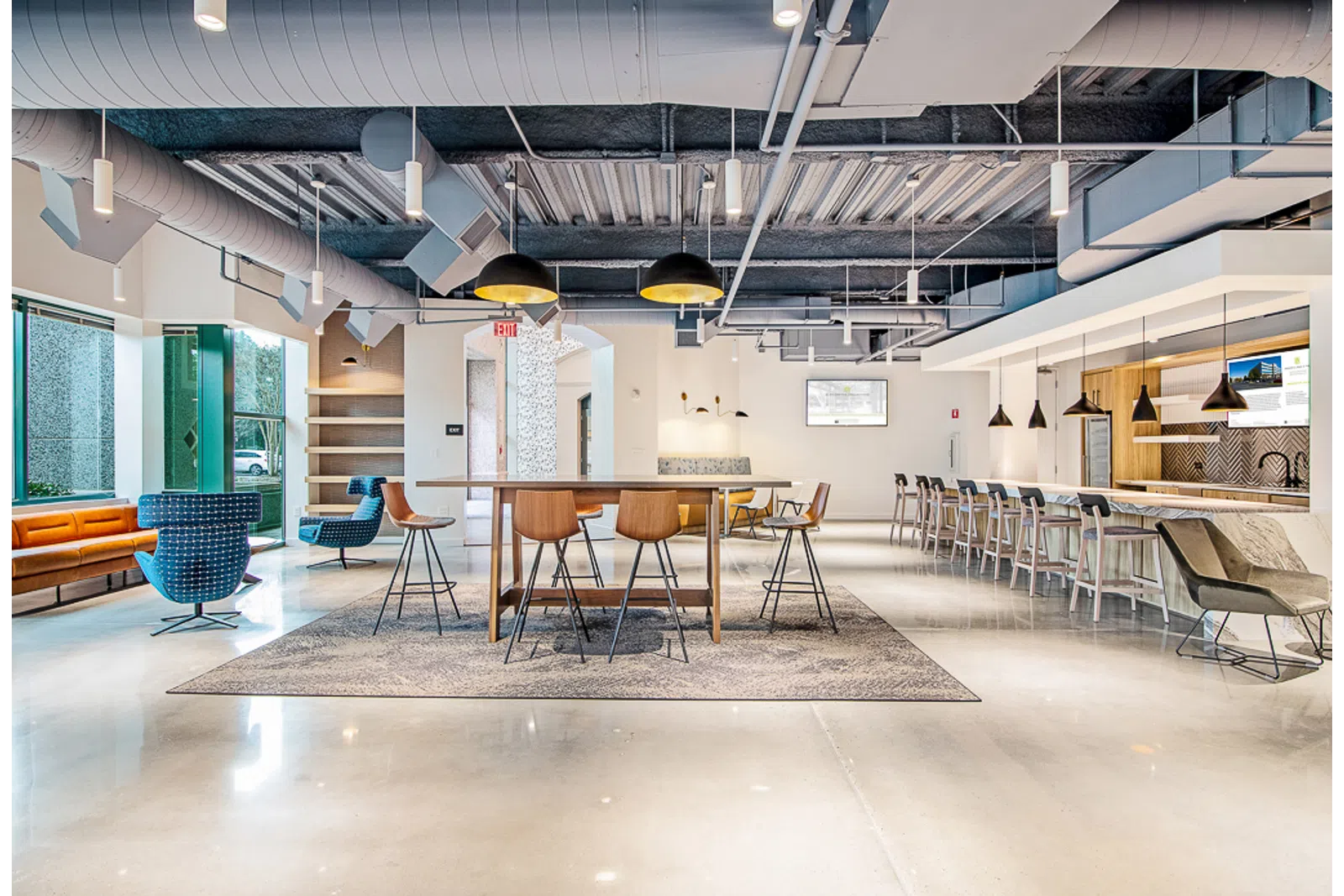 Modern office lounge with a long table, bar stools, comfortable seating, and industrial ceiling design
