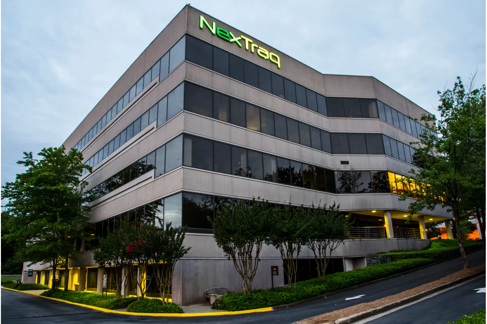 Modern office building with NexTraq logo on top, surrounded by trees and greenery under a cloudy sky