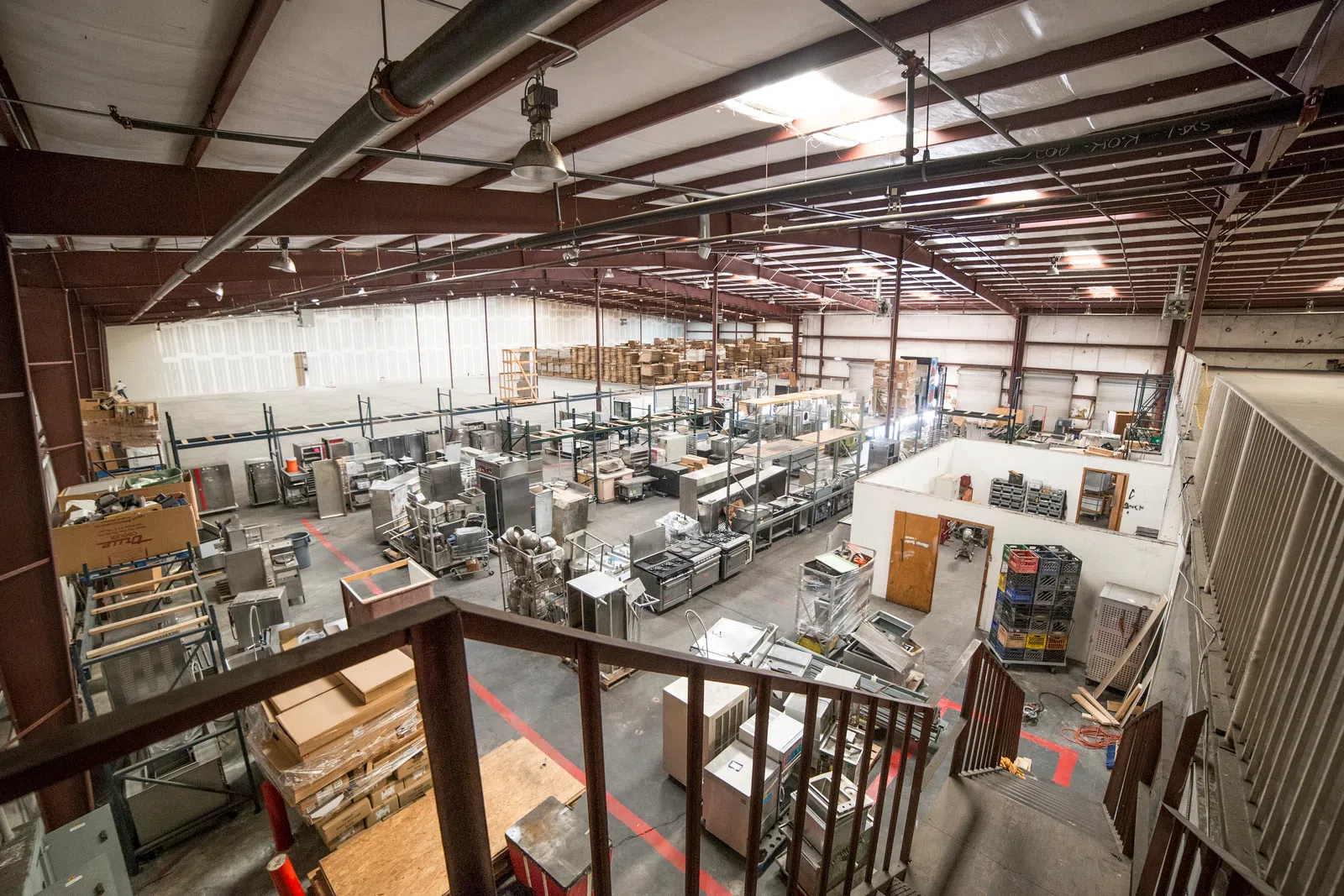 Spacious warehouse interior with industrial shelving, equipment, and boxes organized under a metal roof.