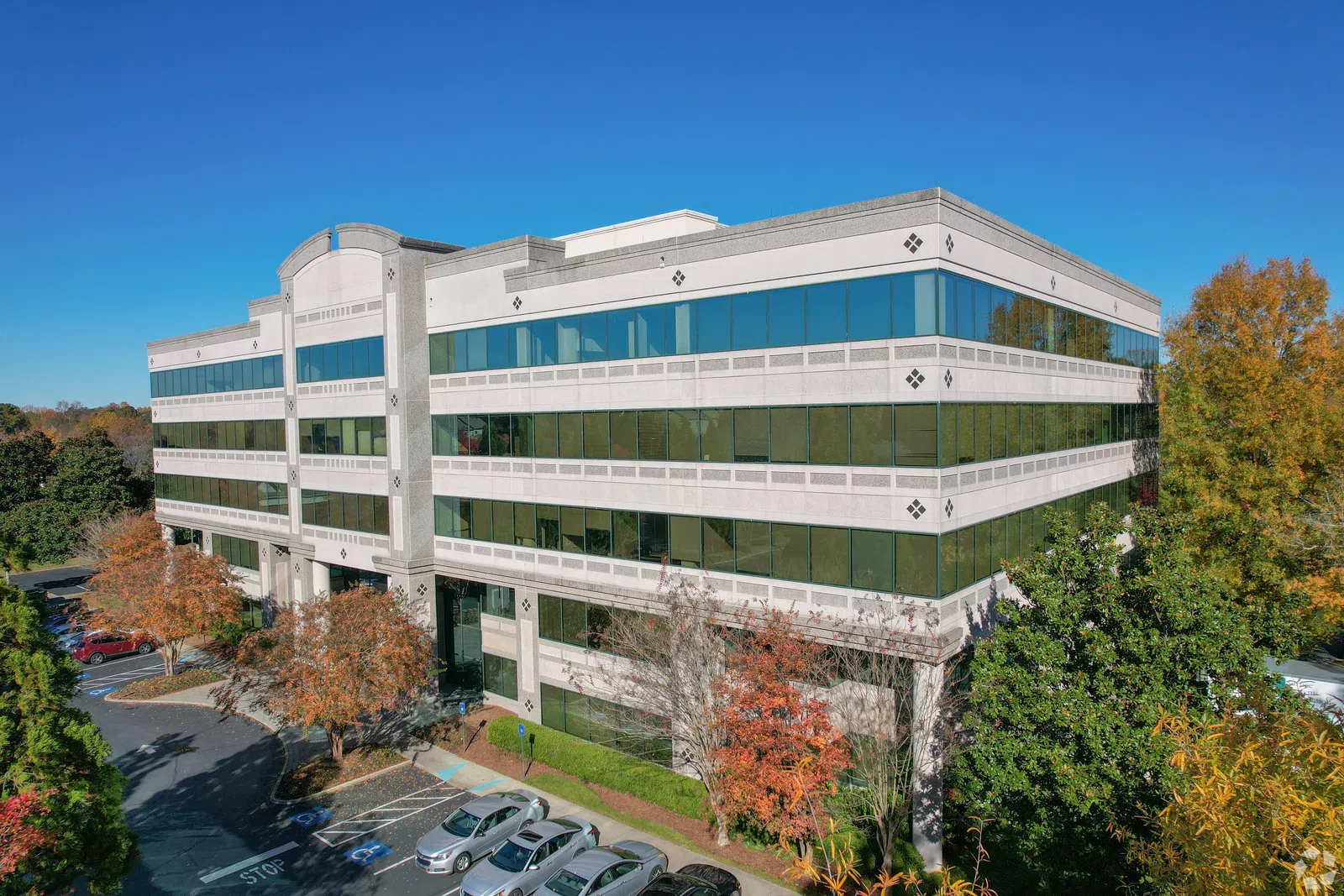 Modern office building with large glass windows surrounded by trees and parked cars under a clear blue sky
