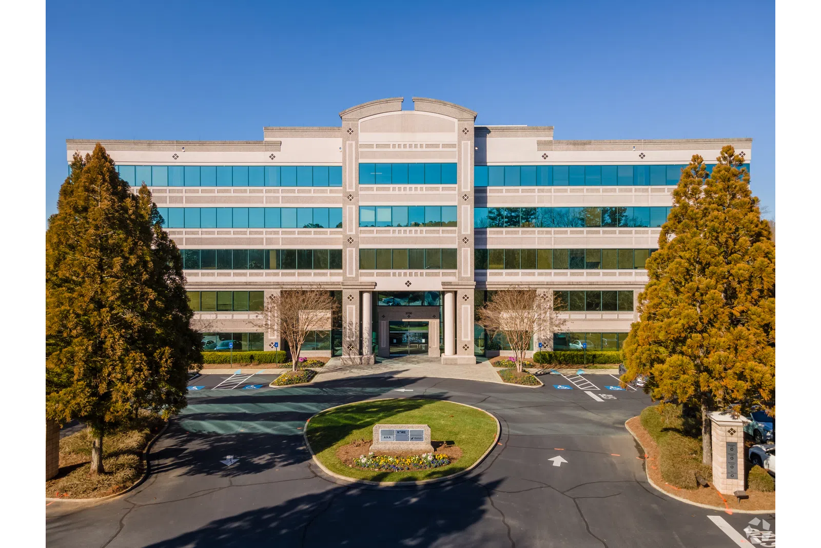 Modern four-story office building with reflective windows, surrounded by trees under a clear blue sky.