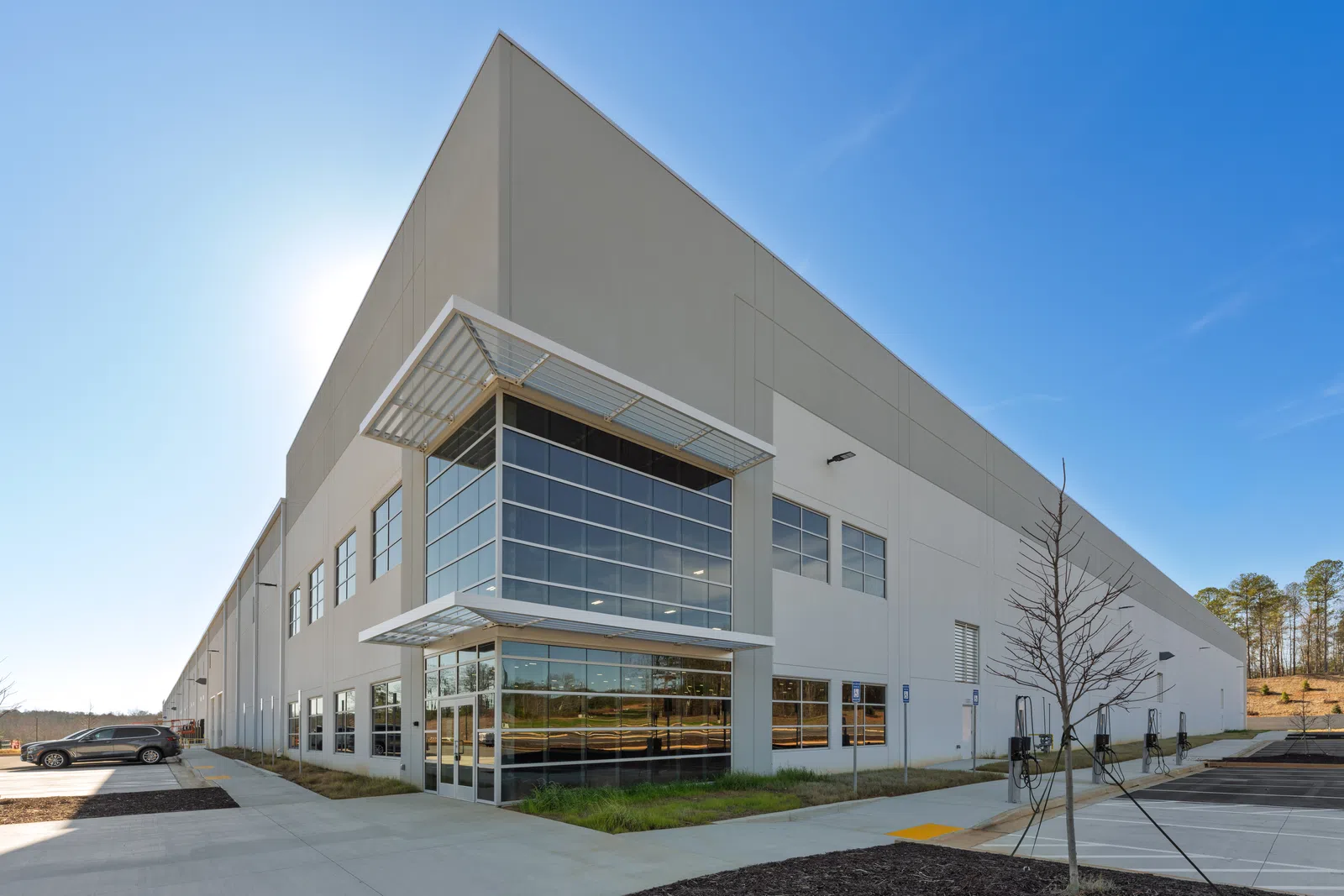 Modern industrial warehouse with large windows and parking lot under a clear blue sky on a sunny day