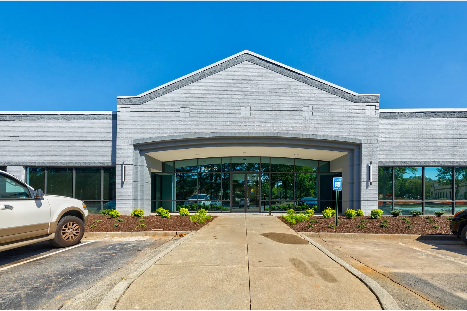 Modern gray brick commercial building entrance with glass doors and parking spaces under clear blue sky