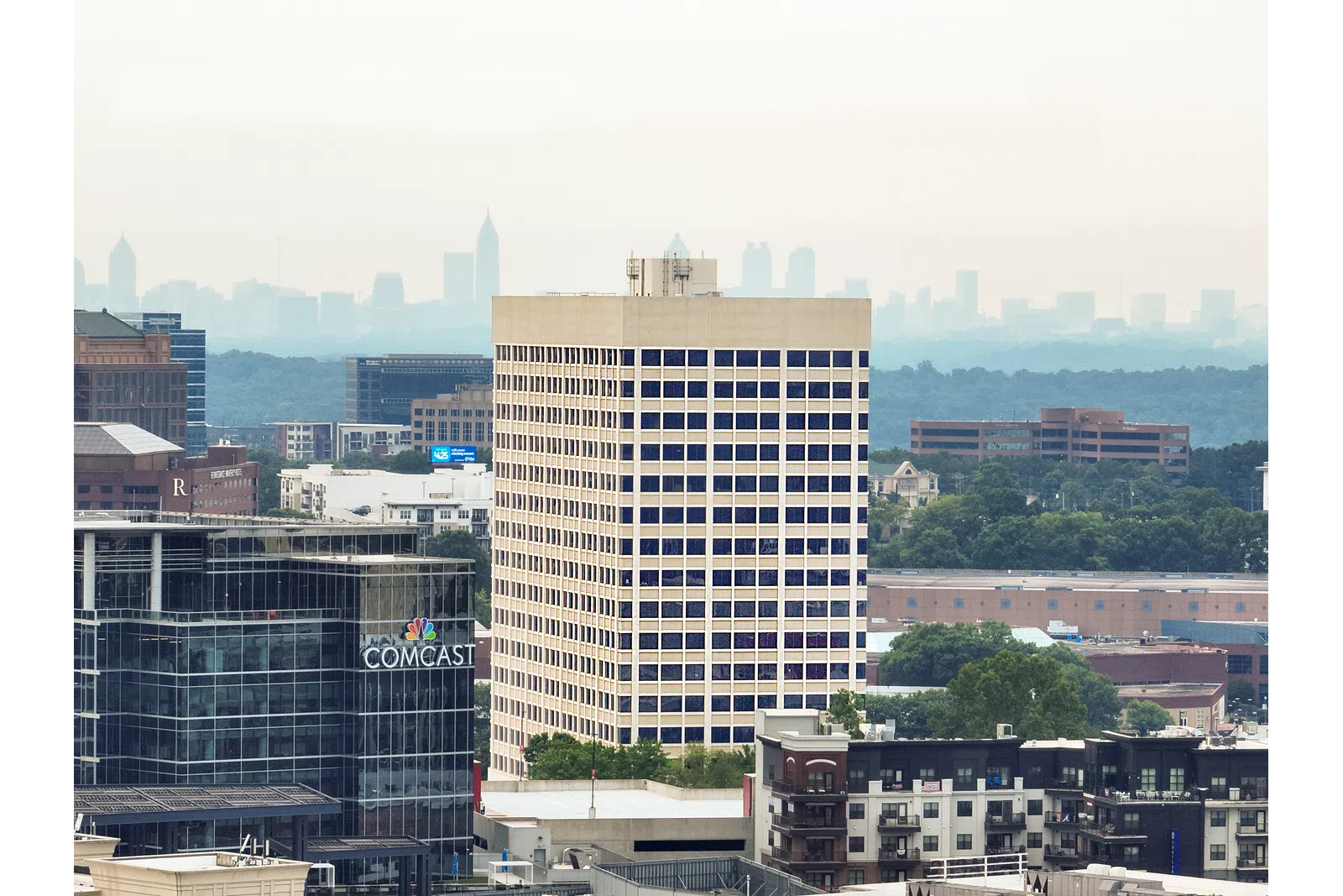 Urban skyline with Comcast building, modern offices, and distant cityscape under a hazy sky.