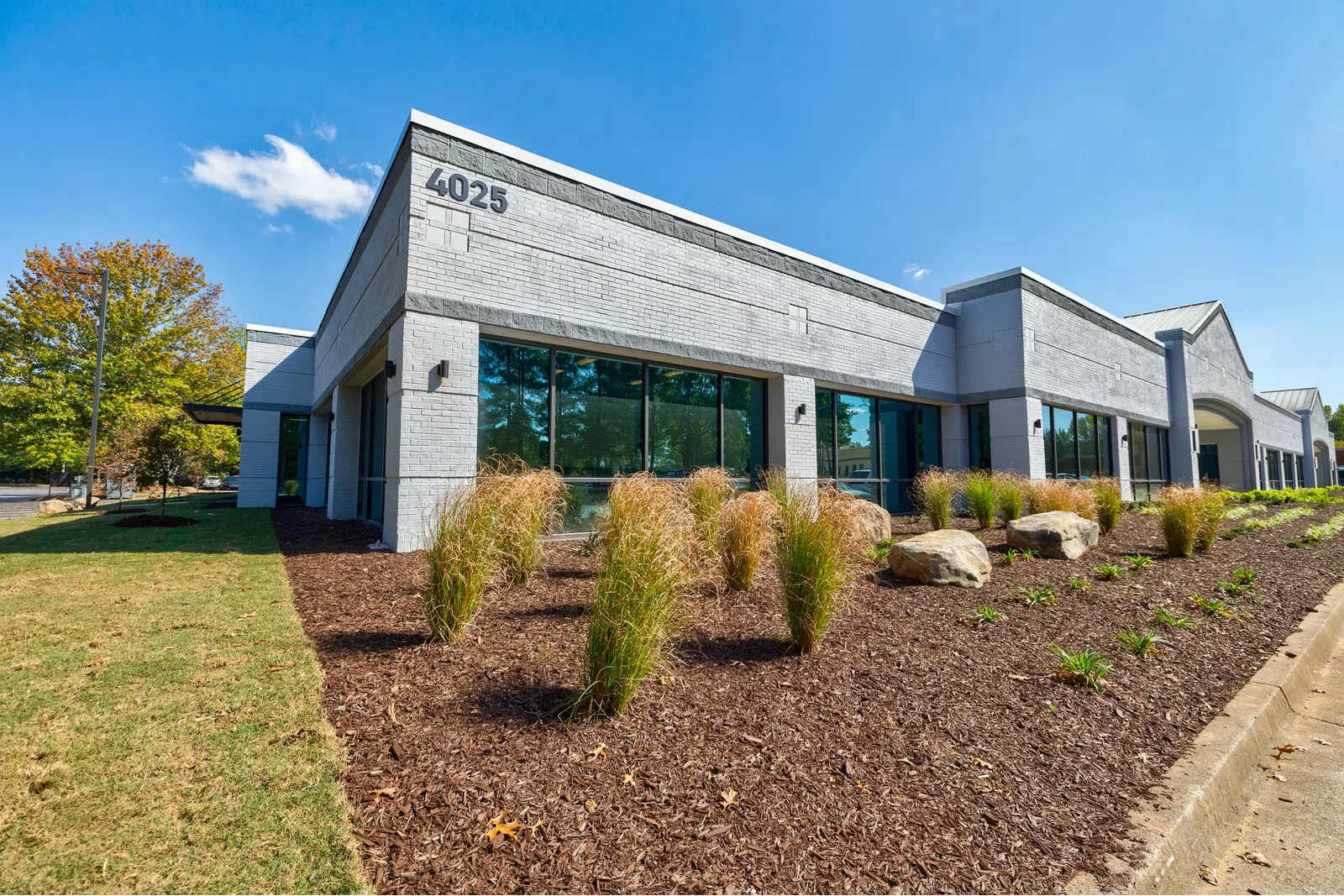 Modern single-story office building with large windows, landscaped garden, and clear blue sky at 4025 address.