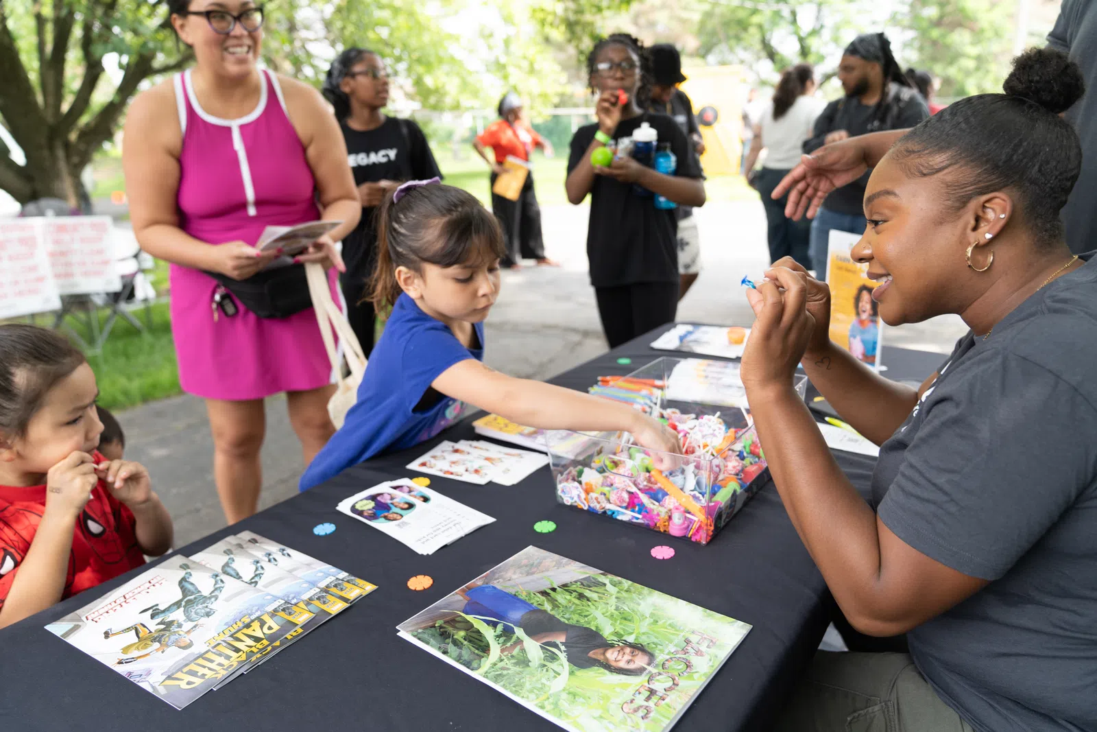 Children and adults engaging at a colorful community event table with crafts and informational materials outdoors.