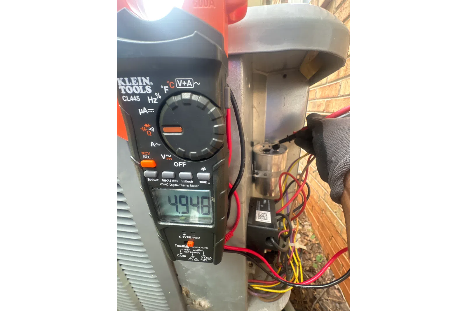 AC Repairs in Tucker Atlanta by The Air Company of GA. HVAC technician using a Klein Tools digital clamp meter to measure electrical current on an outdoor condenser unit.