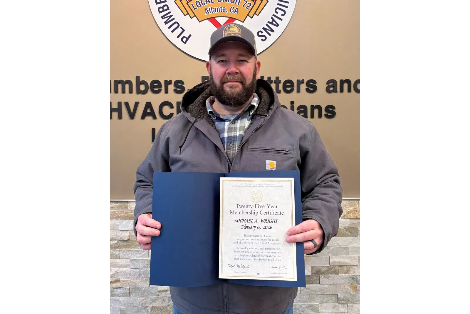 Man holding certificate in front of Plumbers, Pipefitters and Service Technicians union sign on wall