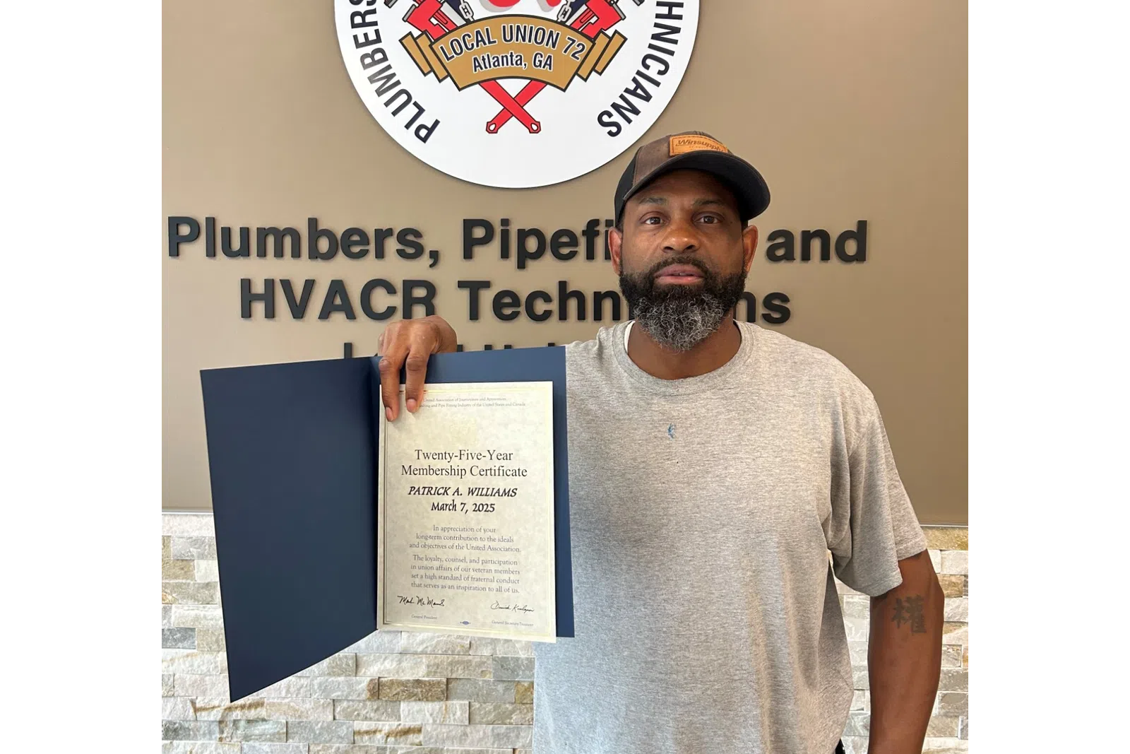 Man holding a certificate standing next to Plumbers and Pipefitters union sign on wall