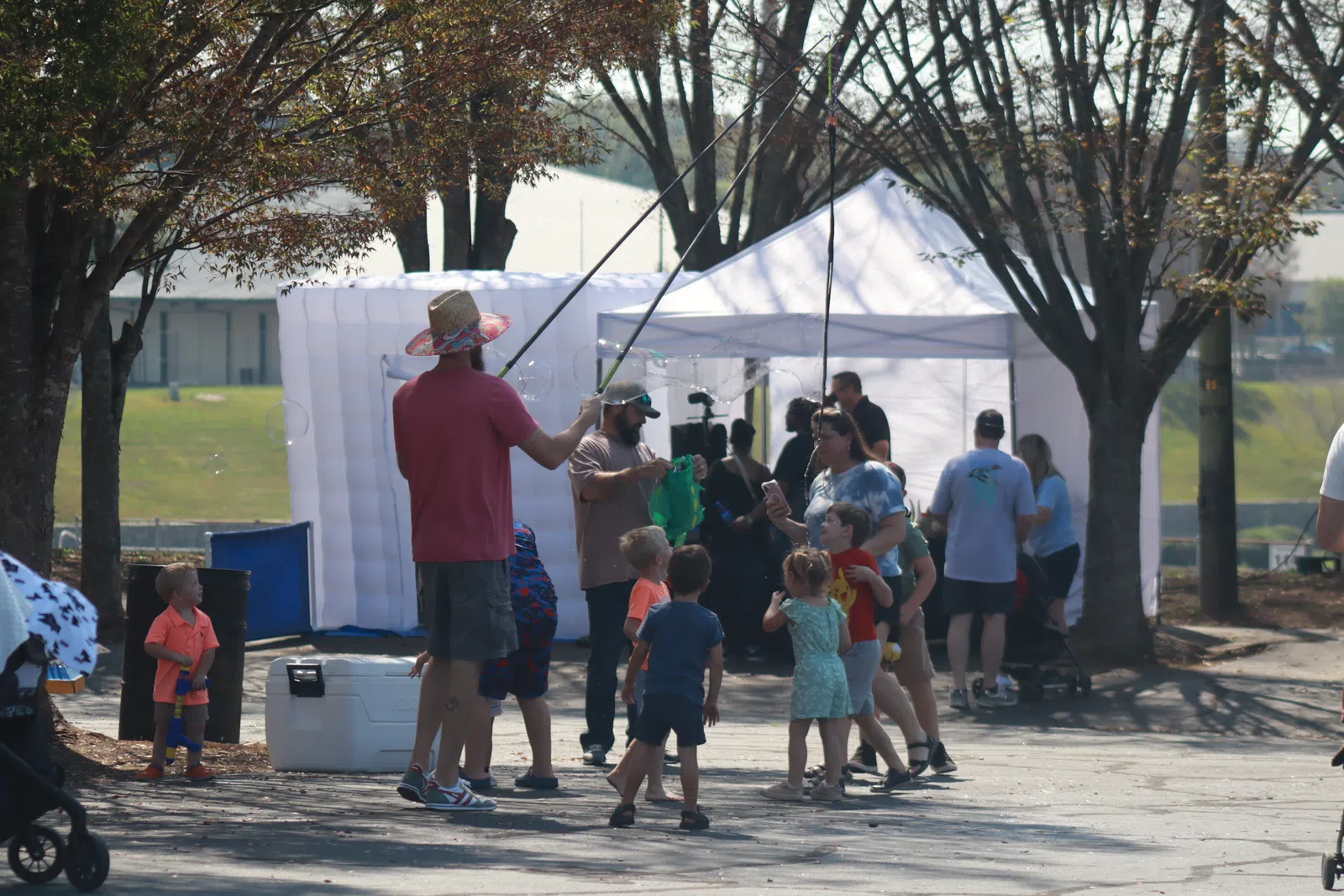 Adults and children gathered outdoors near tents, engaging in a fishing activity on a sunny day with trees around.