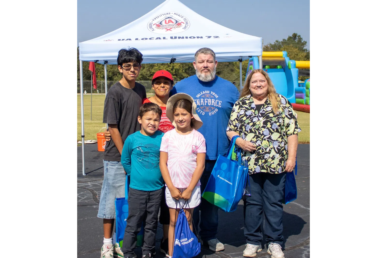 Group of six people posing at an outdoor event with a union tent and inflatable play structure in background.