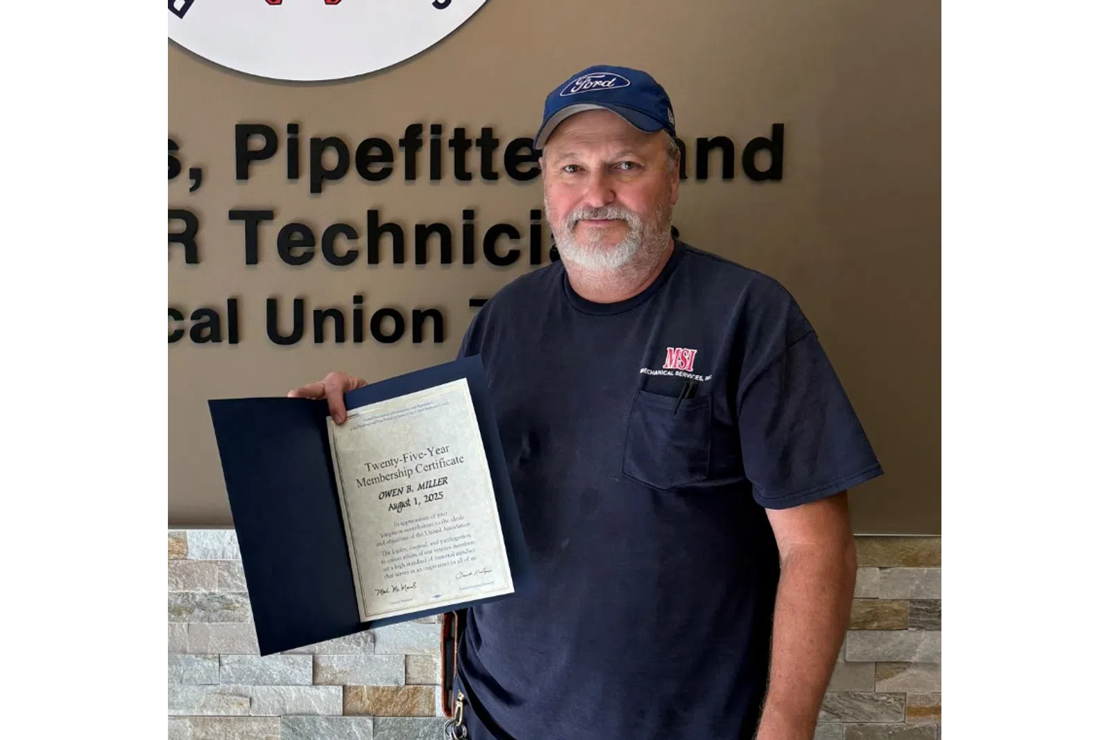 Man standing next to Plumbers and Pipefitters union sign holding a certificate inside a building.