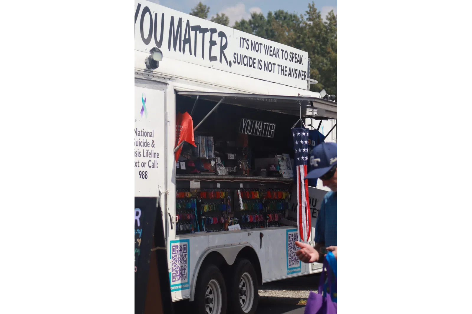 Mobile suicide prevention booth with YouMatter and hotline info, a man walking nearby under blue sky