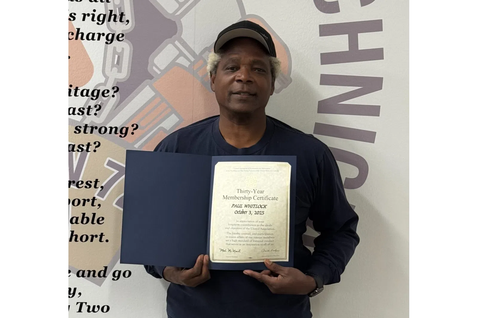 Man holding a thirty-year union membership certificate standing in front of a wall with union-related text and logo.