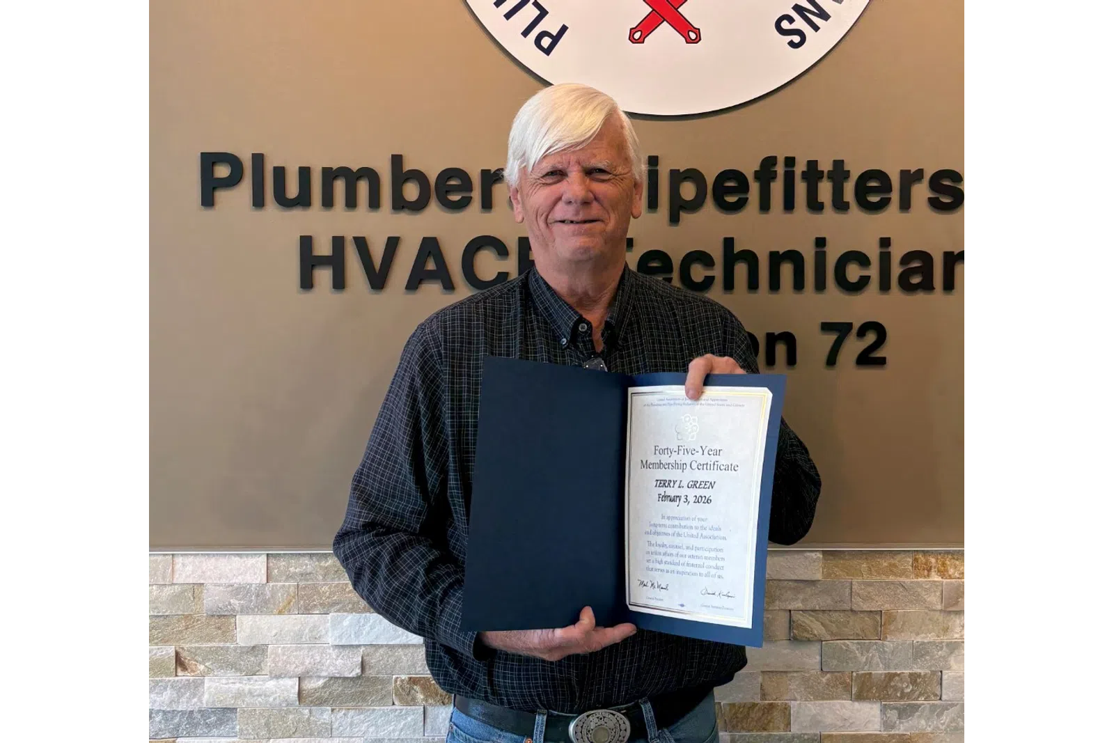 Man holding certificate standing in front of Plumbers and Pipefitters Local Union 72 sign in office