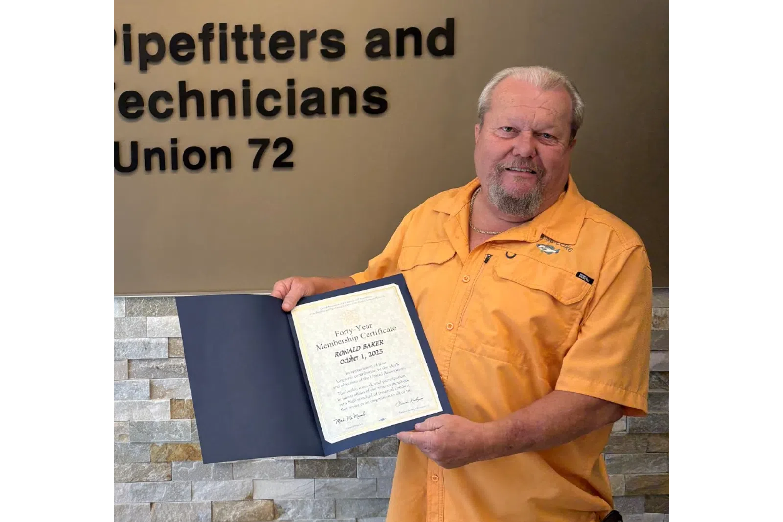 Man holding certificate standing next to Plumbers, Pipefitters and HVACR Technicians Local Union 72 sign indoors.