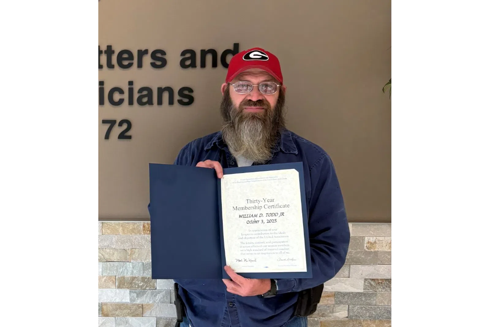 Bearded man in red hat holding certificate standing next to Plumbers, Pipefitters & HVACR Technicians Local Union 72 logo.