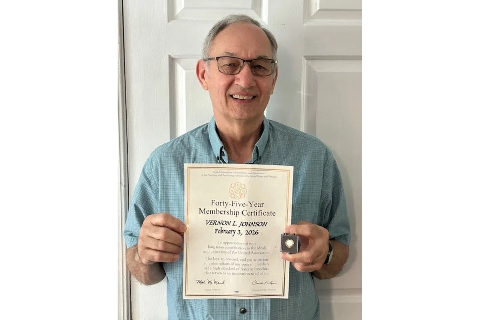 Man wearing glasses and blue shirt holding a forty-five year membership certificate and a pin, smiling at the camera.