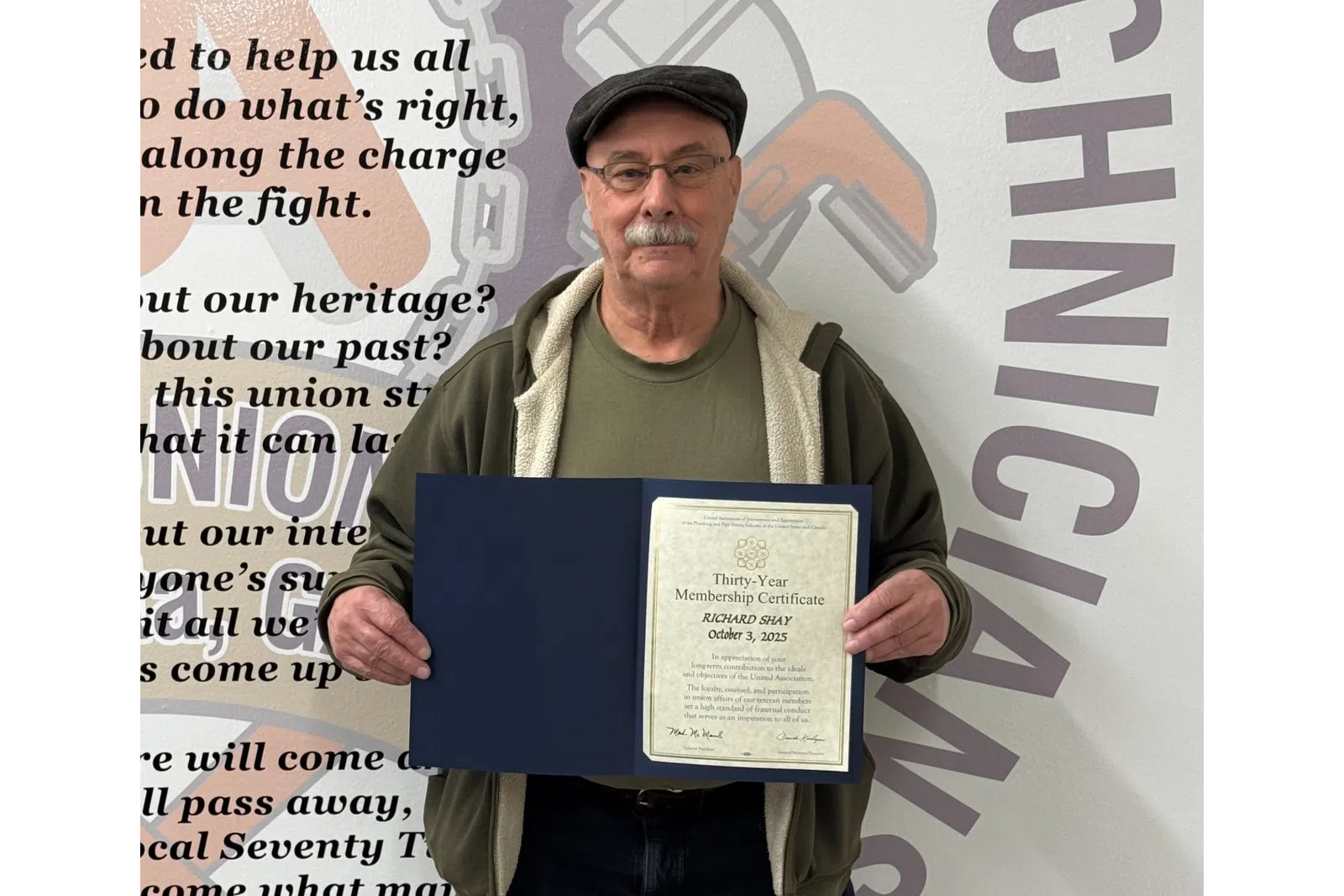 Man holding a thirty-year membership certificate standing in front of a wall with union text and graphics.