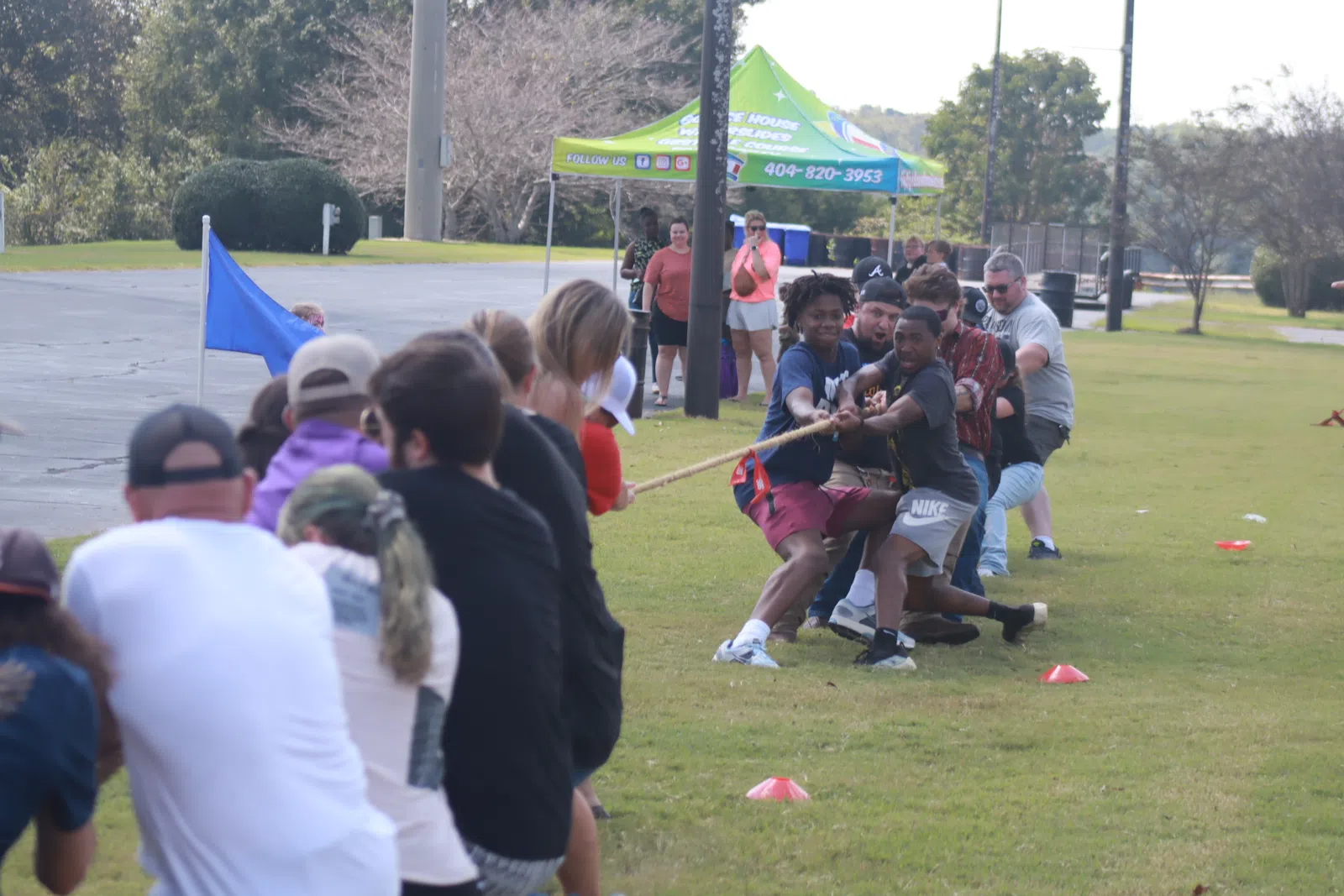 People participating in an outdoor tug-of-war game on a grassy field during a sunny day.