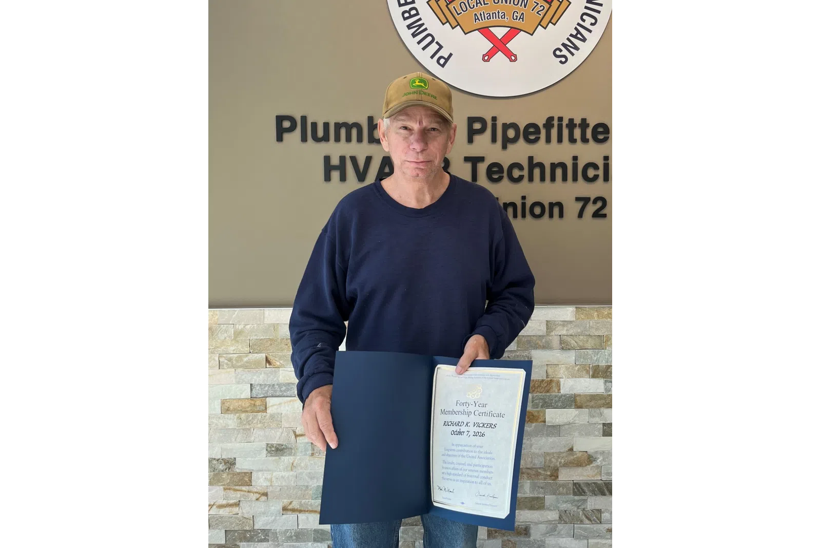 Man in a cap holding a certificate stands by a wall with a Plumbers and Pipefitters Union 72 sign and overlaid text.