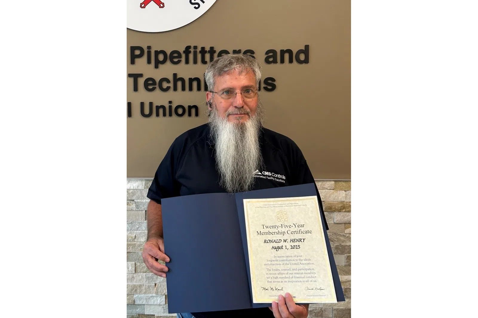 Man with long beard holding a certificate in front of Plumbers, Pipefitters & HVACR Technicians Local Union 72 sign.