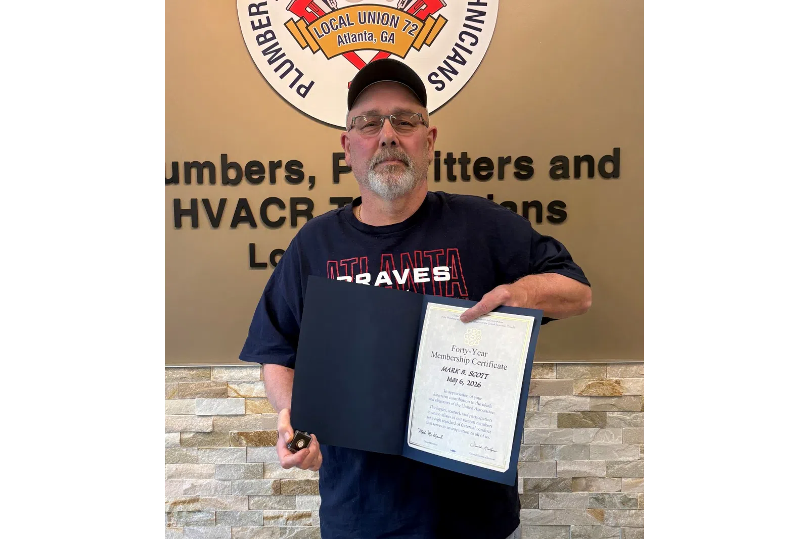 Man wearing a cap and glasses holding a certificate and key standing by a union service technicians logo and text.