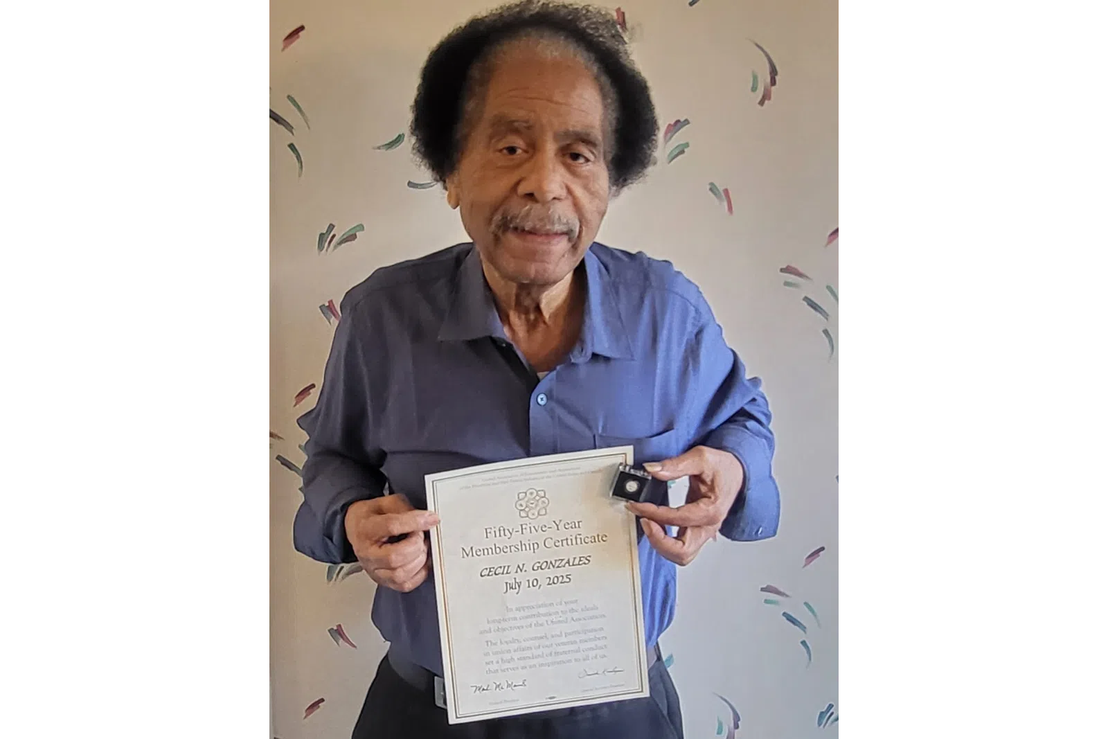 Elderly man holding a Fifty-Five-Year Membership Certificate and a pin for Cecil N. Gonzales, dated July 10, 2025.