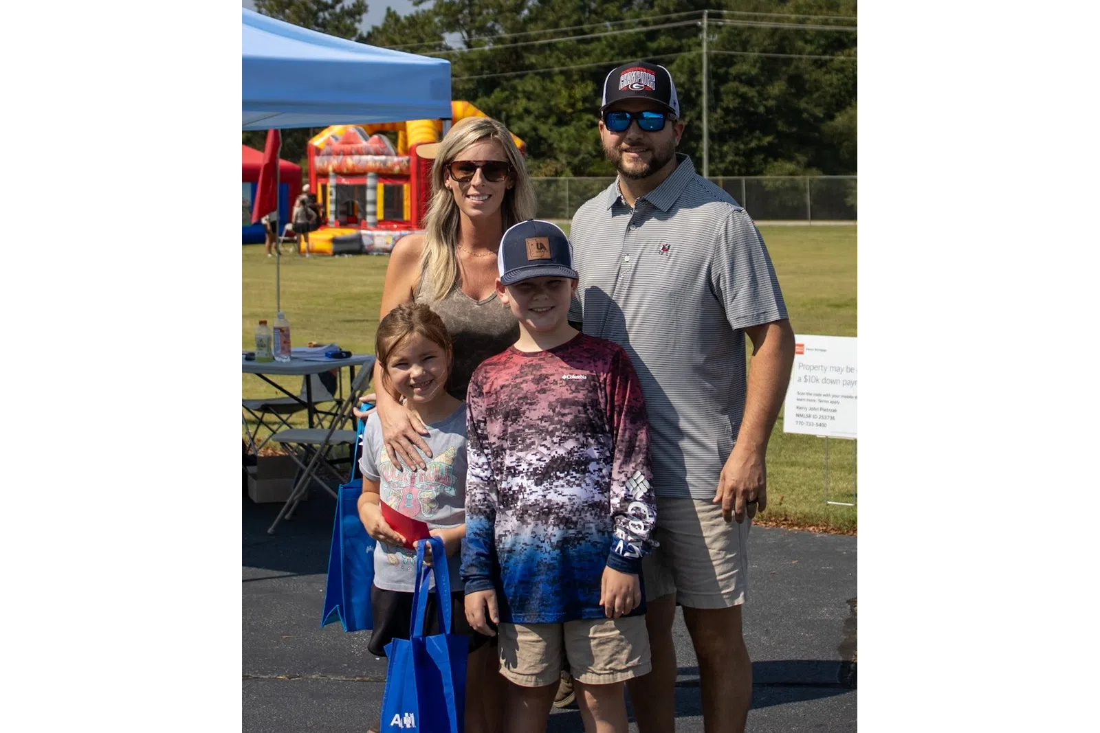 Family of four posing at outdoor festival with tents, inflatable bounce houses, and sunny weather