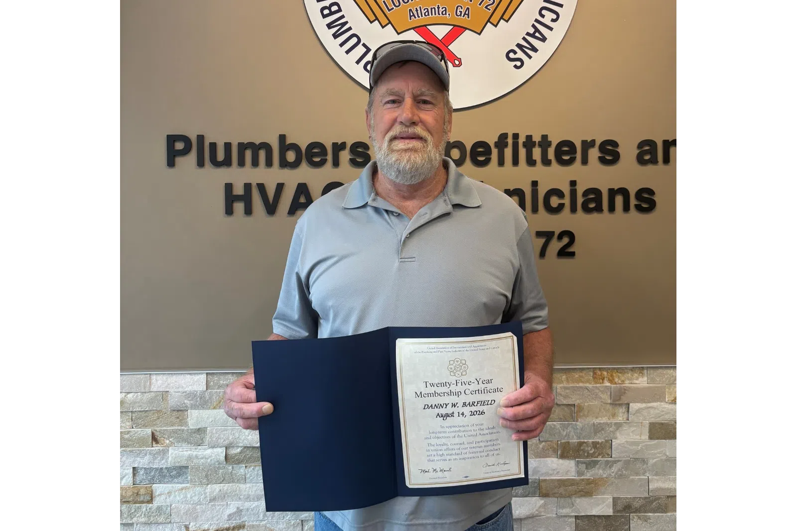 Man holding a certificate standing next to Plumbers and Pipefitters Local Union 72 sign on wall.